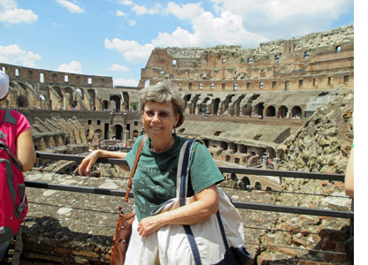 Photo shows Dona smiling and standing in front of a railing overlooking the inside of the Coliseum.